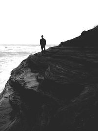 Silhouette man standing on rock by sea against clear sky