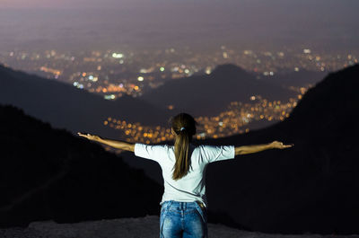 Rear view of woman standing against cityscape at dusk