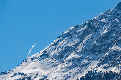 Low angle view of snowcapped mountains against clear blue sky