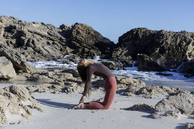 Rear view of shirtless man sitting on rock at beach