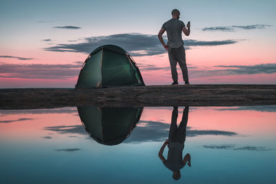 Rear view of man and tent and reflecting on water at sunset