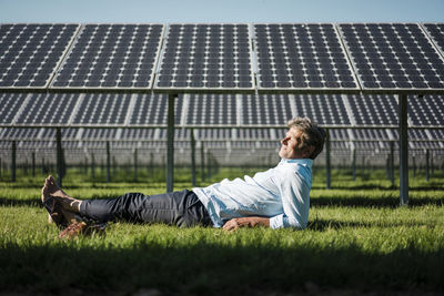 Mature man lying barefoot on meadow, solar plant