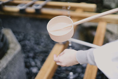 Cropped image of person washing hand with bamboo ladle