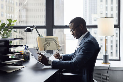 Serious businessman working while sitting against window in office