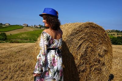 Smiling mid adult woman standing by hay bale on field against sky