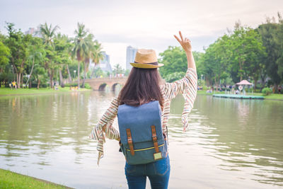 Rear view of woman with backpack standing by lake in park