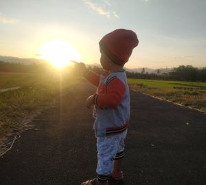 Rear view of boy standing on field against sky during sunset