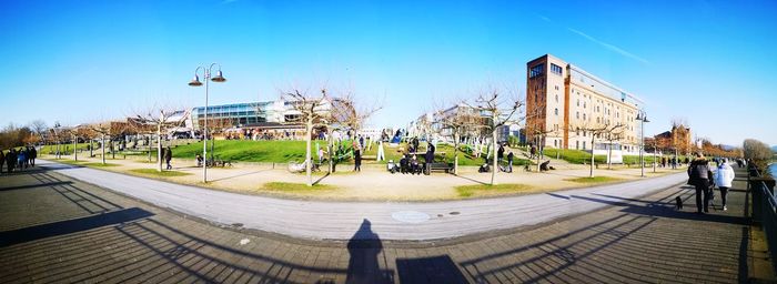 People on footpath in city against clear blue sky