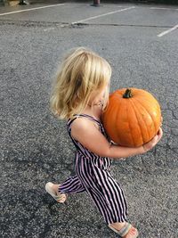 High angle view of girl holding pumpkin while standing outdoors