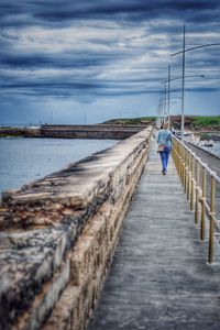 Rear view of man walking on jetty leading to lake