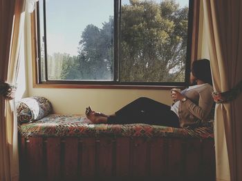 Young woman relaxing on bed by window at home