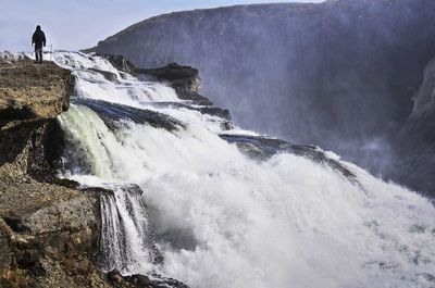 Rear view of man standing on cliff by waterfall