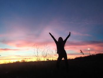 Silhouette woman with arms outstretched standing against sky during sunset