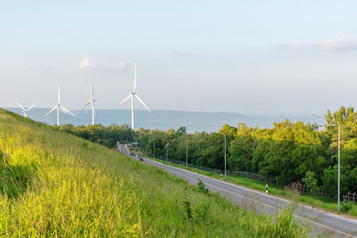 Windmill on field by road against sky