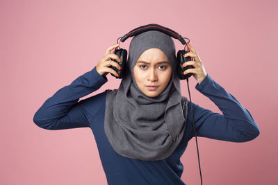 Young woman listening music against pink background