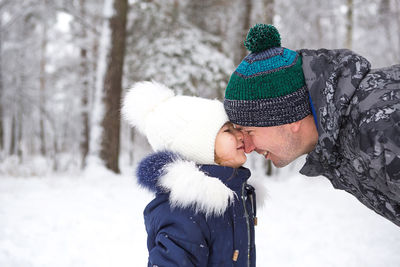 Dad and daughter look at each other closely in warm clothes, hats with a pompom on the street 