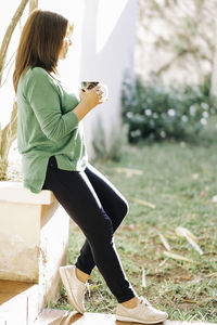 Side view of woman sitting outdoors holding a hot beverage