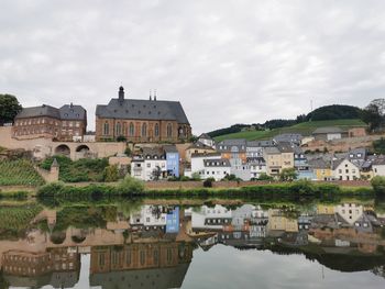 Buildings by river against sky in town