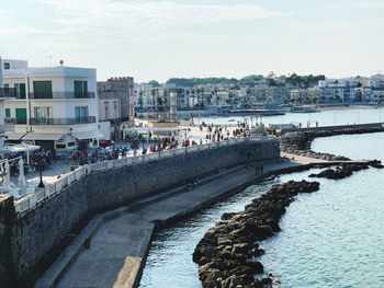 People on river by buildings in city against sky