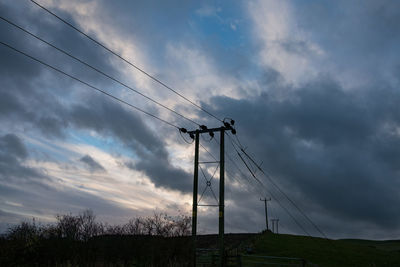 Low angle view of silhouette electricity pylon against sky