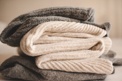 Stack of knitted wool textile sweaters clothes on white blanket in bed at home room close up.