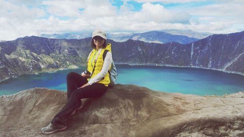 Portrait of young woman sitting on rock formation against lake