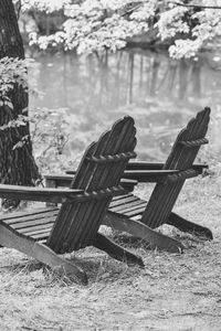 Empty adirondack chairs by pond in forest