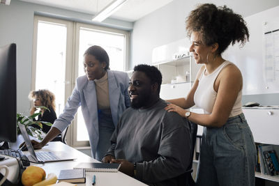 Happy female colleague encouraging male employee sitting at desk in office