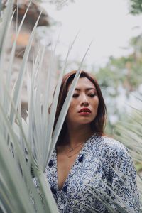 Young woman looking away while standing against plants in park