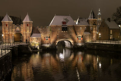 Bridge over river by illuminated buildings against sky at night