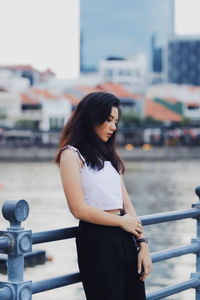 Side view of thoughtful young woman standing on footbridge by river