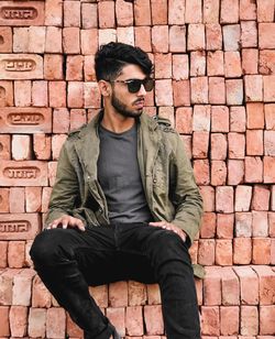 Young man wearing sunglasses while sitting on stacked bricks
