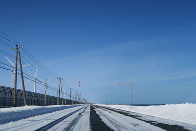 Road amidst snow covered landscape against blue sky