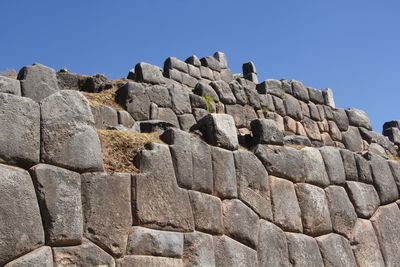 Low angle view of stone wall against clear blue sky