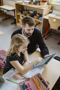 Girl studying through tablet pc by male teacher in classroom