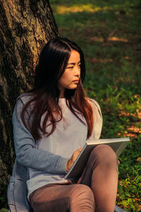 Young woman looking away while sitting on tree trunk