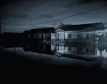 Houses by lake and buildings against sky at dusk