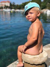 Full length of naked baby boy sitting by lake