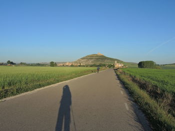 Road amidst field against clear blue sky