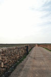 Woman standing by stone retaining wall on roadside while photographing landscape against sky