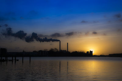 Smoke emitting from factory against sky at sunset