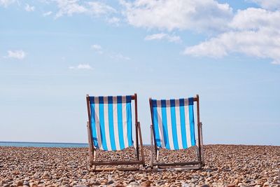 Deck chairs at beach against sky