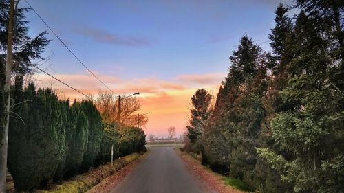 Road amidst trees against sky during sunset