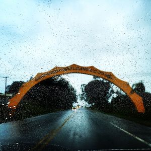 Arch over road against sky on rainy day seen from car windshield