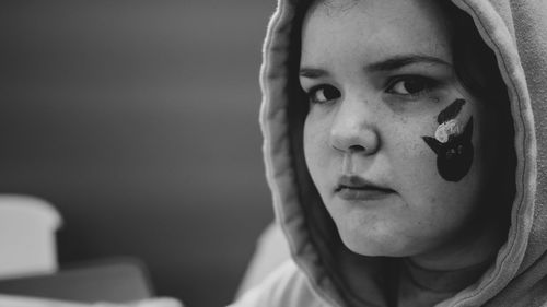 Close-up portrait of girl with face paint wearing hoodie sitting at home