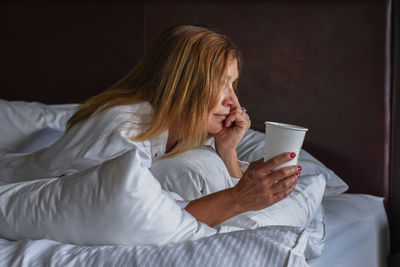 Woman with cup lying on bed at home