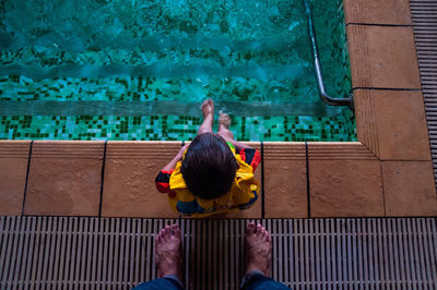 Low section of father standing by son sitting at poolside