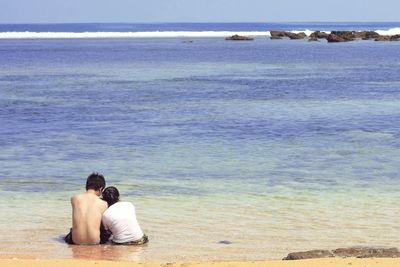 Rear view of couple sitting at beach against sky