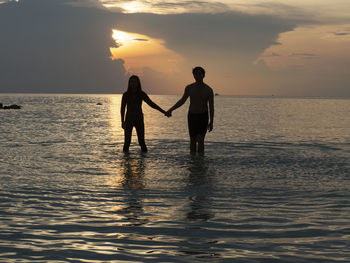Silhouette couple standing in sea against sky during sunset