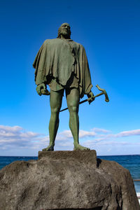 Rear view of statue on rock by sea against sky